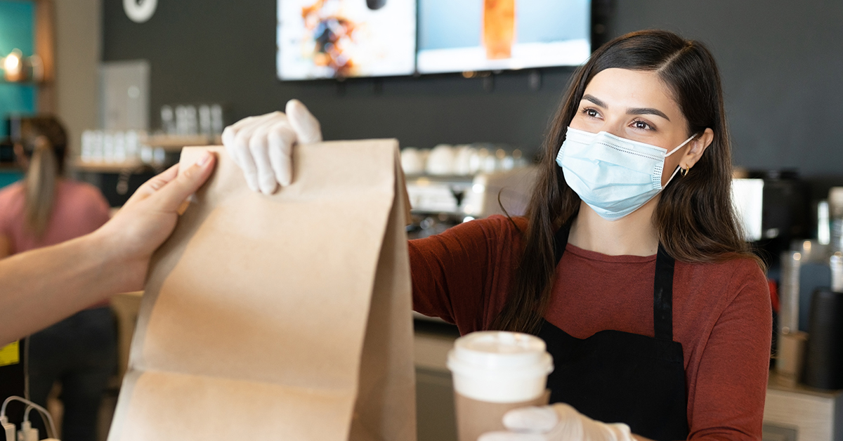 woman wearing mask giving bag and coffee to customer